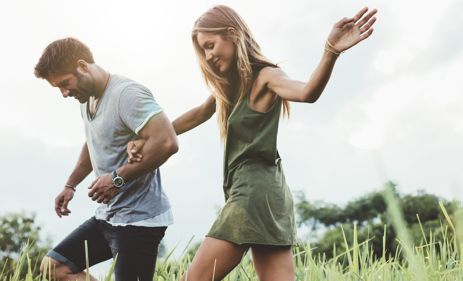 Outdoor shot of young couple walking through meadow hand in hand. Man and woman talking walk through grass field in countryside.